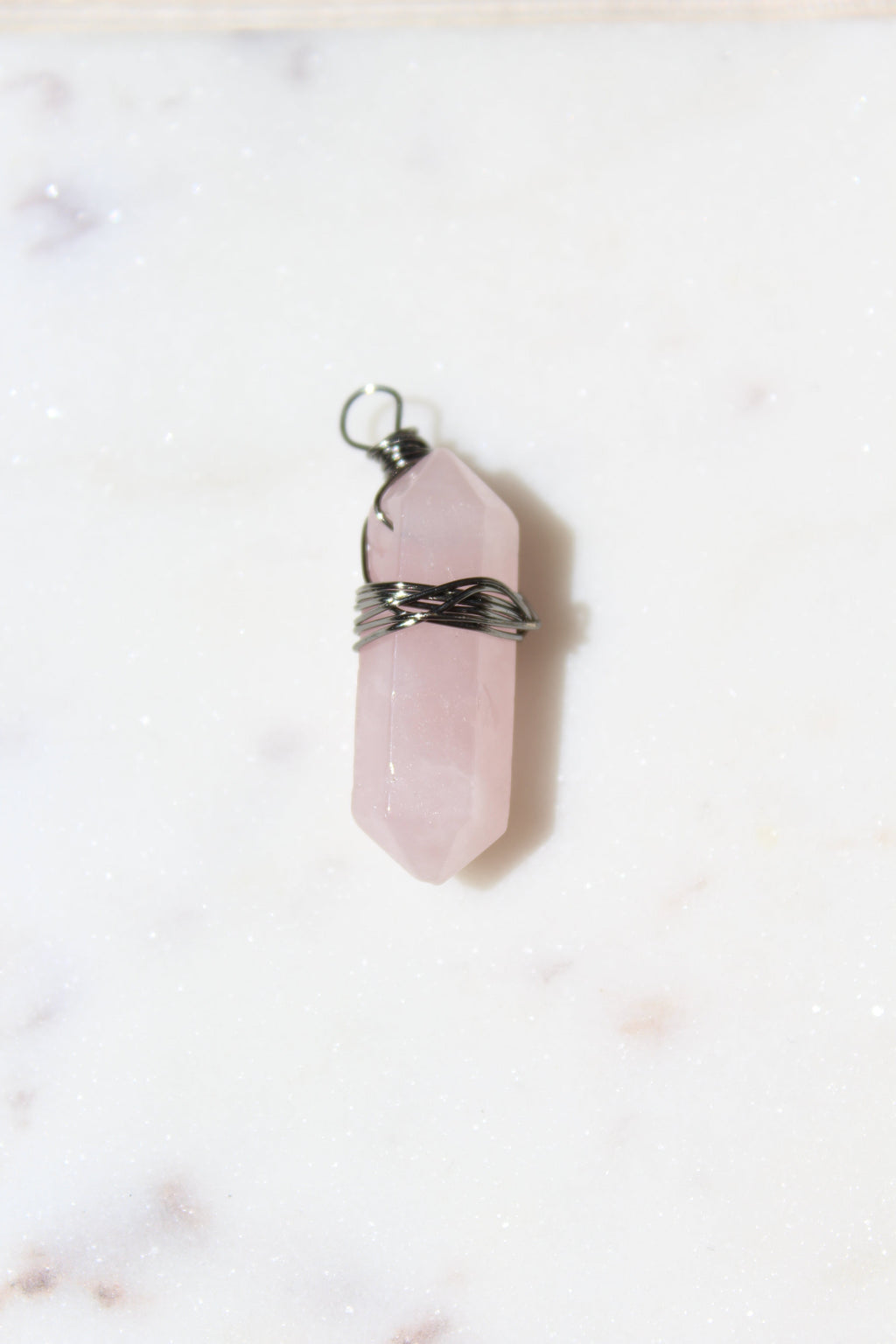 Pink crystal pendant with silver chain on a light marble background