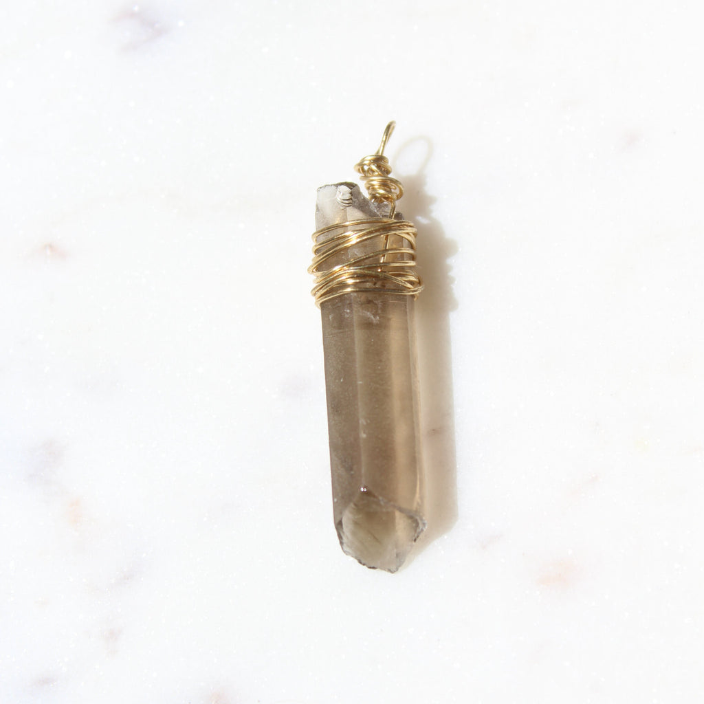 Smoky crystal pendant with gold wire wrapping on a light marble background
