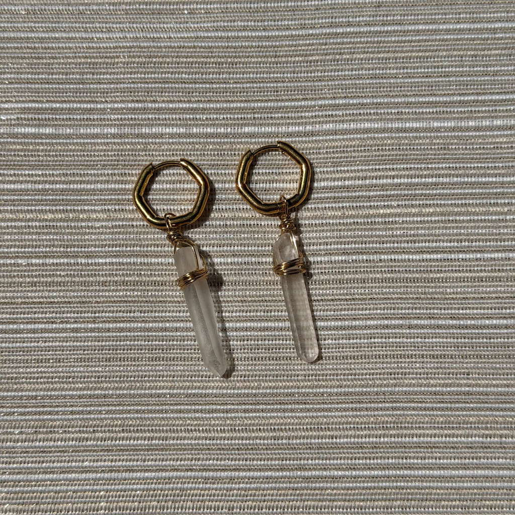 Gold hoop earrings with clear crystal drops on a textured gray background