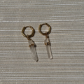 Gold hoop earrings with clear crystal drops on a textured gray background