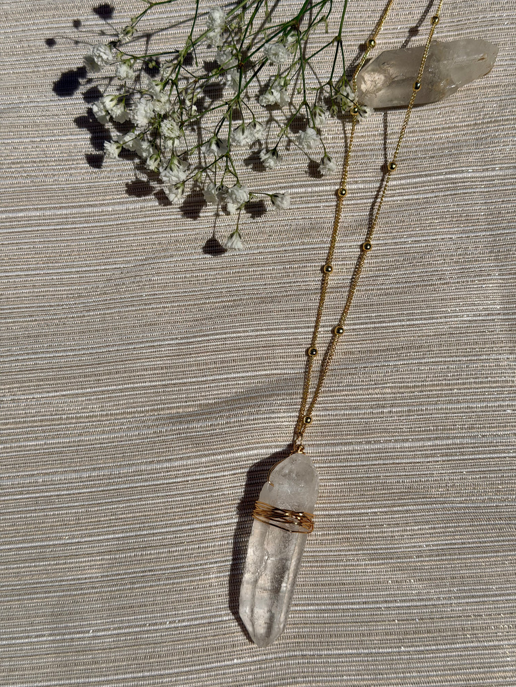 Necklace with a clear crystal pendant on a textured surface with small flowers.