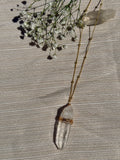 Necklace with a clear crystal pendant on a textured surface with small flowers.